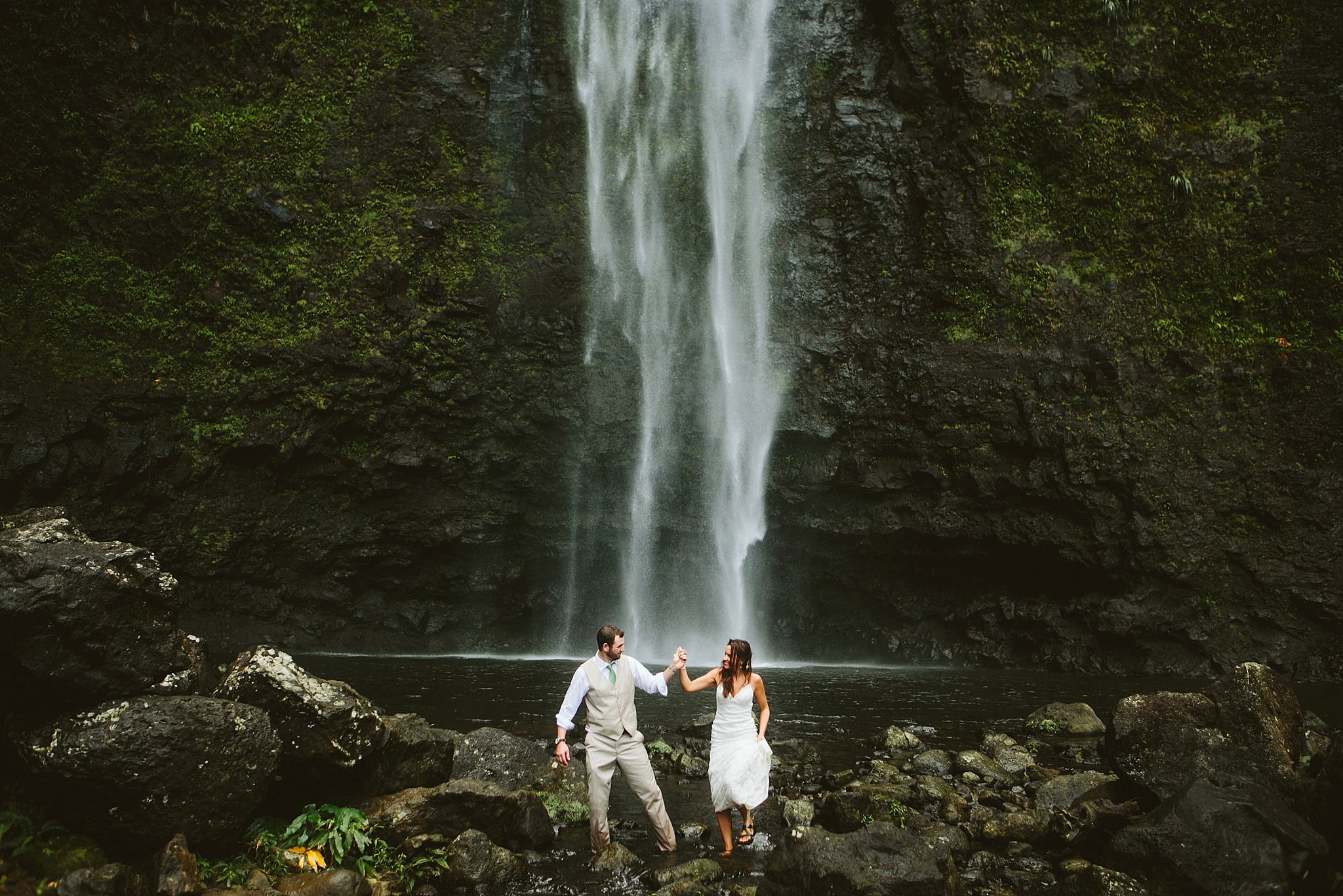 Hanakapiai Falls Kauai HI Elopement Photos Bride and Groom Walking through River Holding Hands