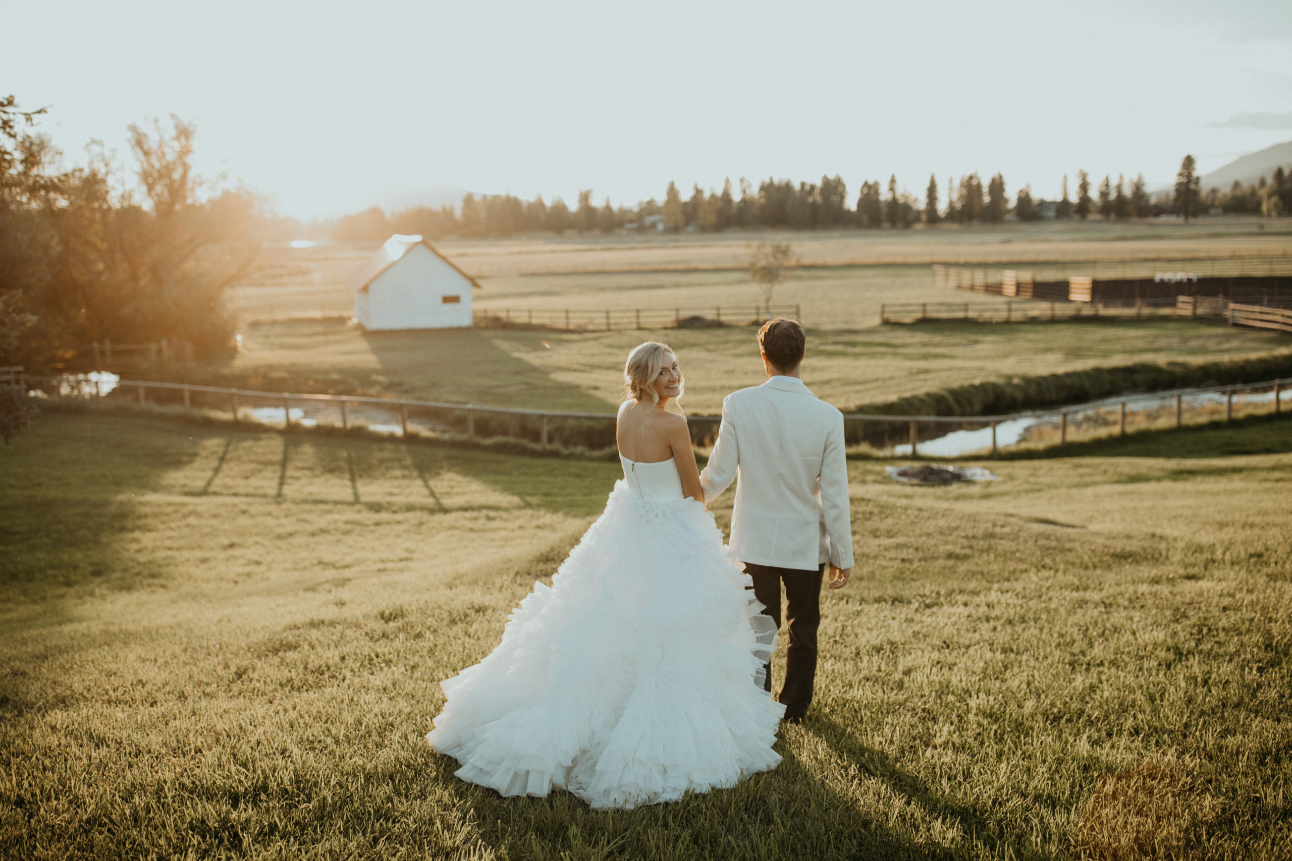 Whimsical Bride and Groom walking hand and hand in a field at sunset in Whitefish MT