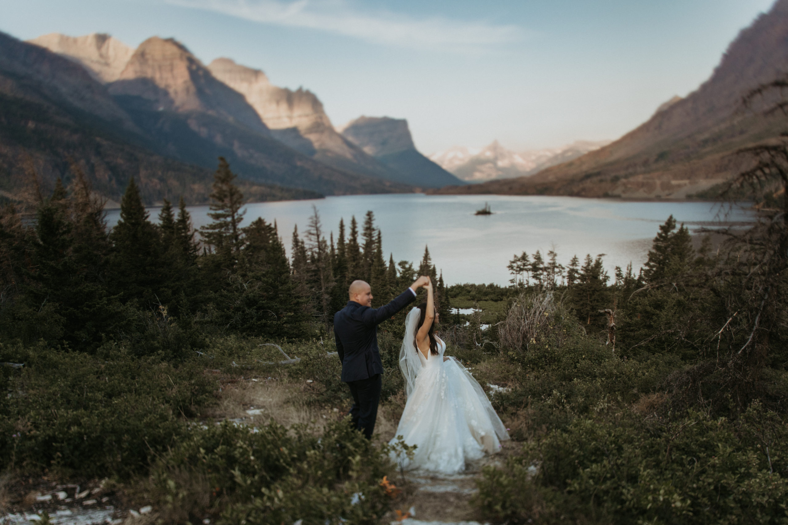 Bride and groom dancing by the lake in the mountains of Glacier National Park at sunrisee